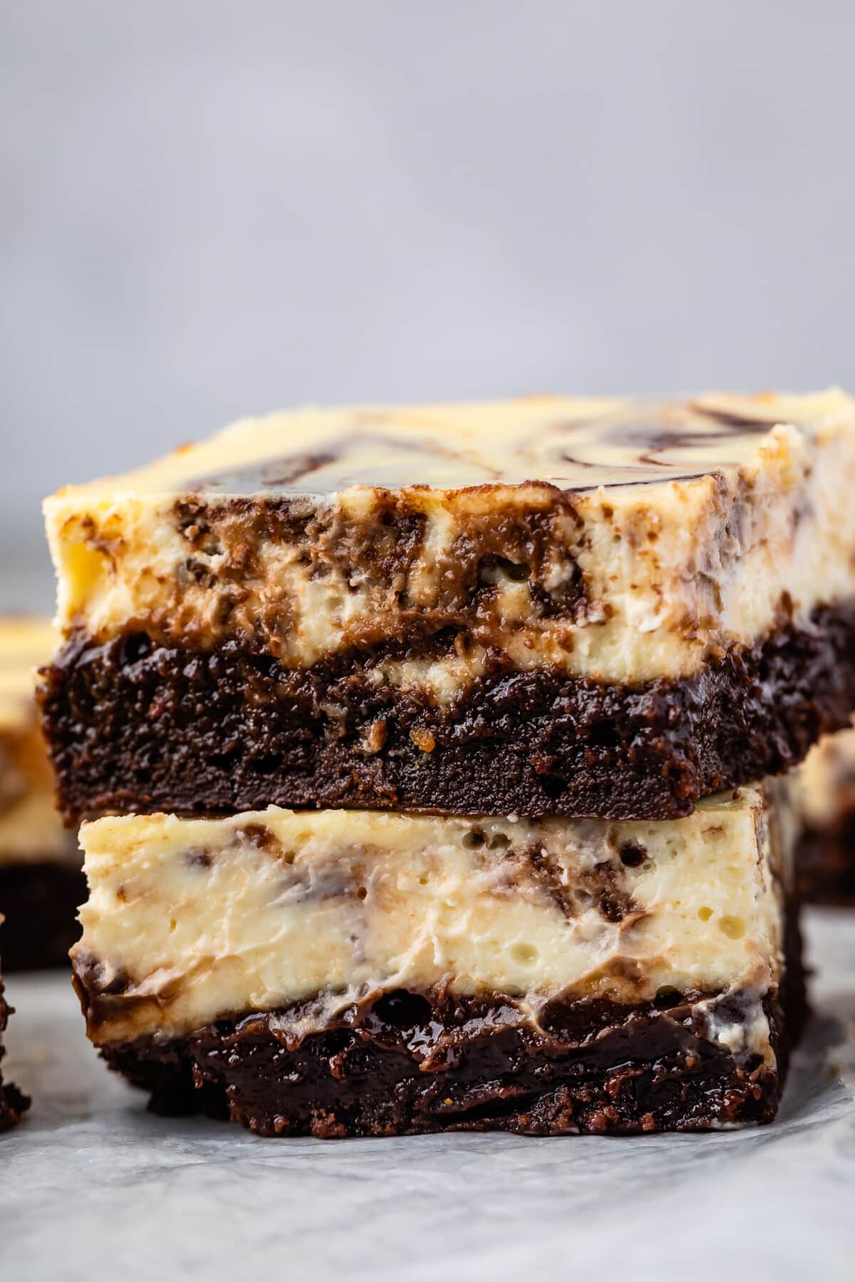 stacked square slices of brownies with a layer of cheesecake on top