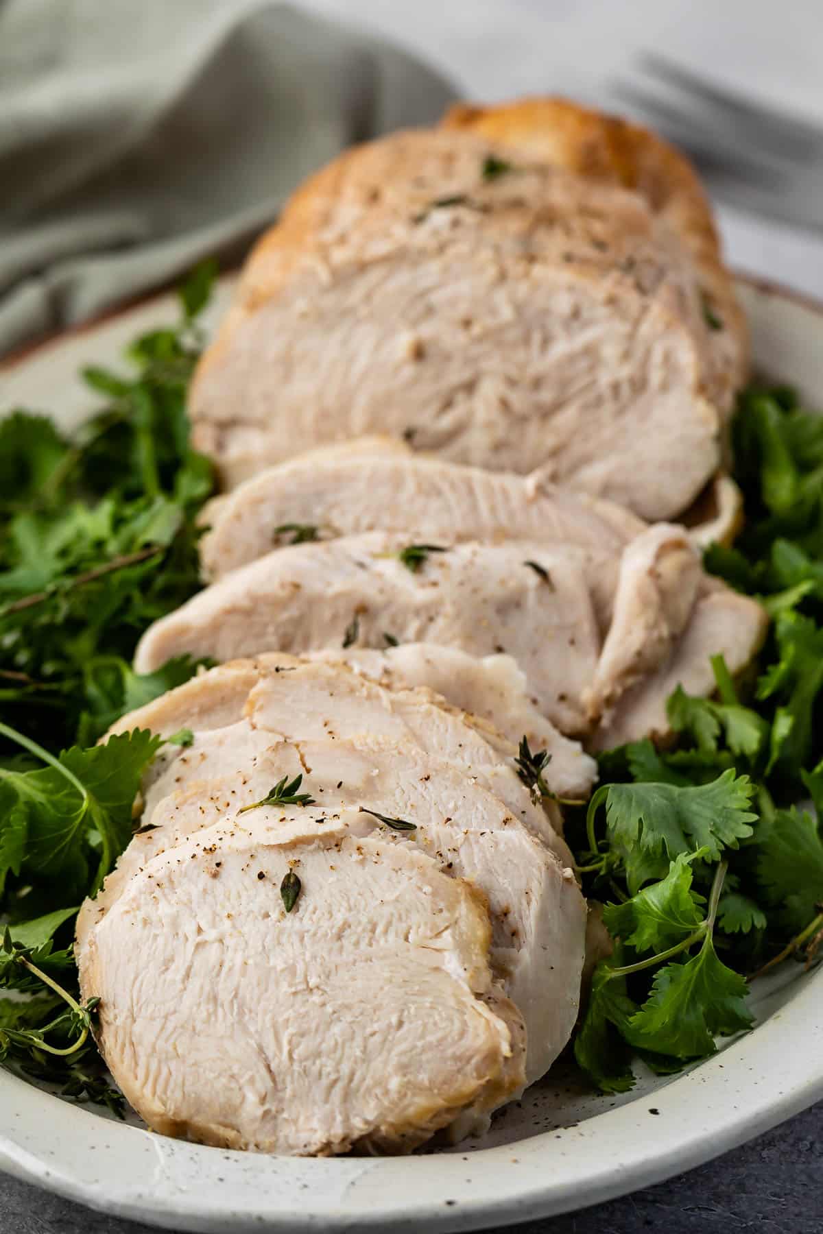 turkey cut into slices on a white plate surrounded by greens