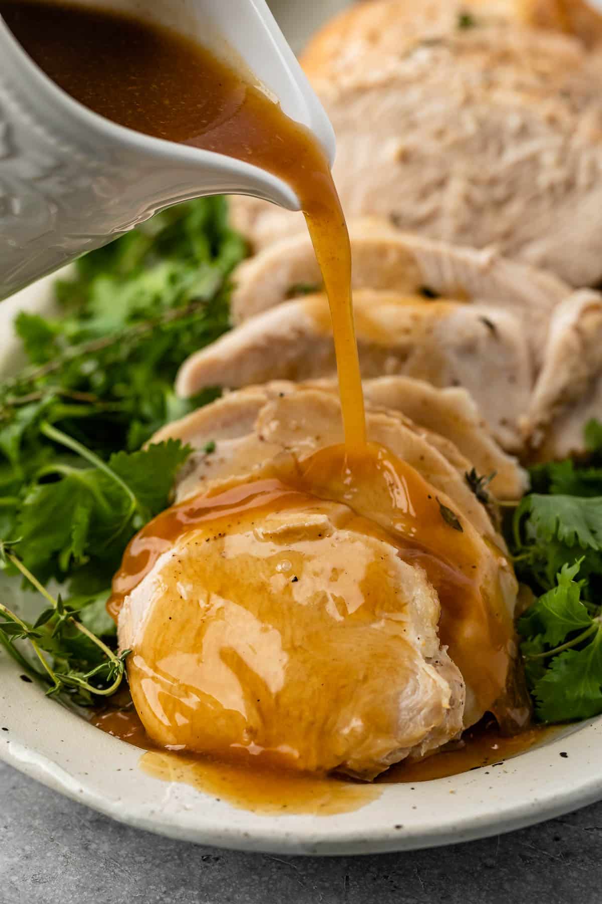 turkey cut into slices on a white plate surrounded by greens and gravy being poured on the turkey