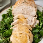 turkey cut into slices on a white plate surrounded by greens