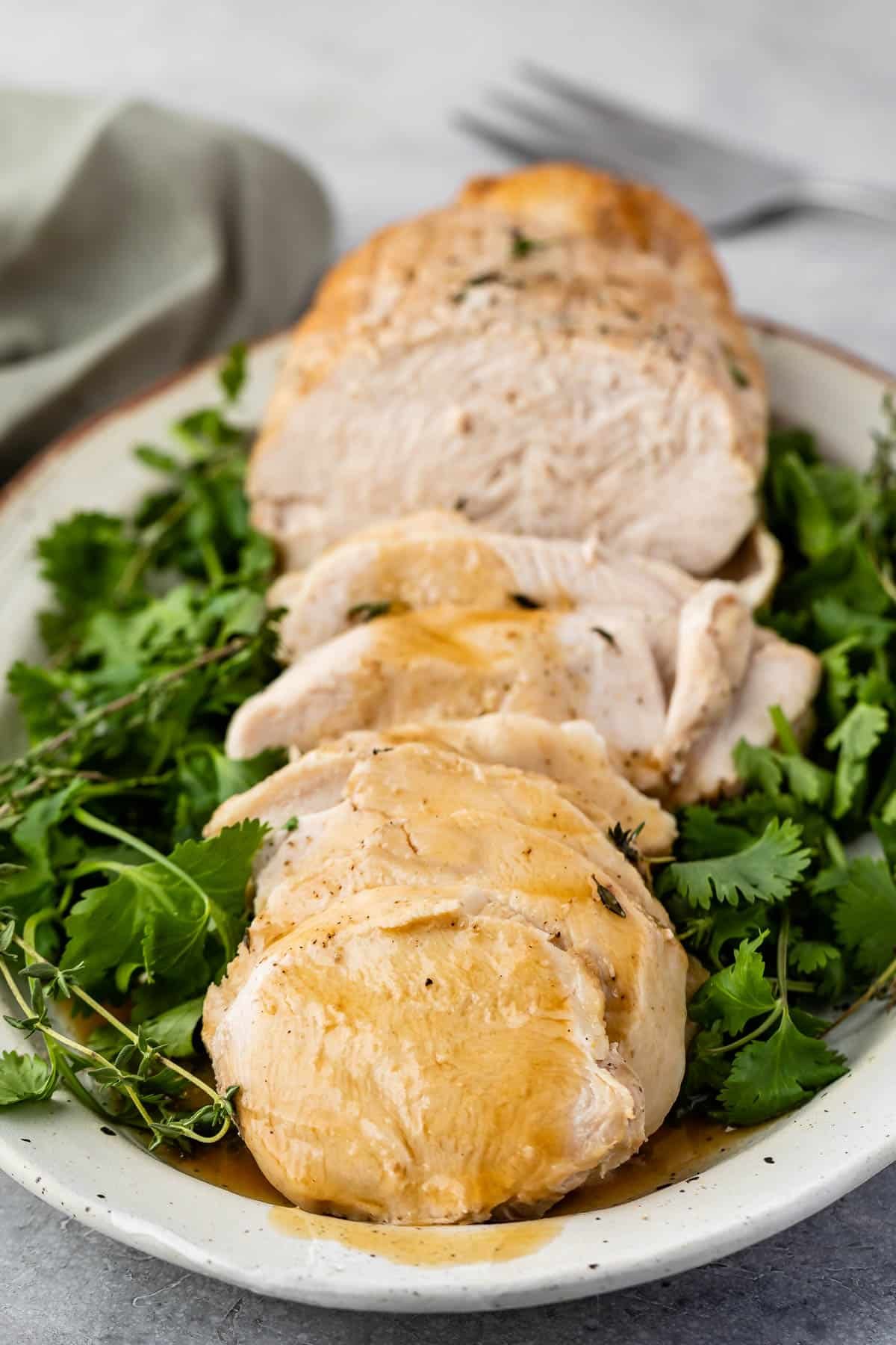 turkey cut into slices on a white plate surrounded by greens