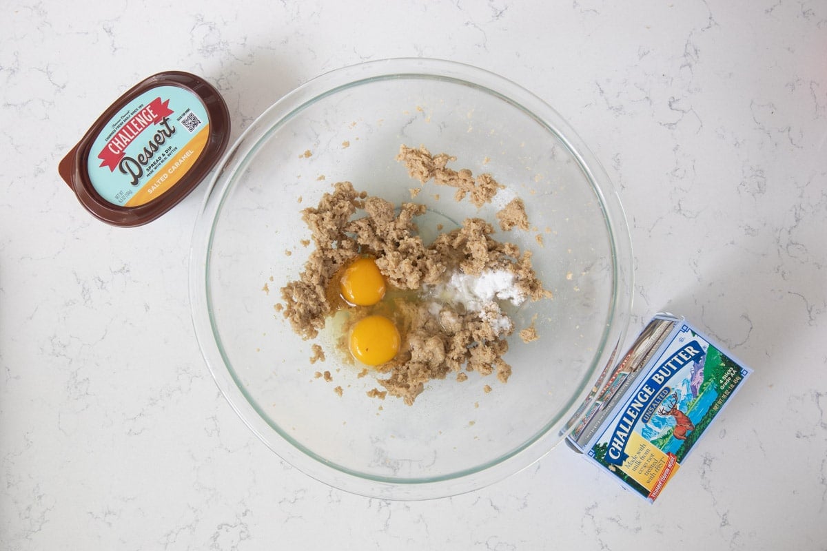 creamed butter and brown sugar with eggs and baking soda in glass bowl on counter with butter and dessert spread.