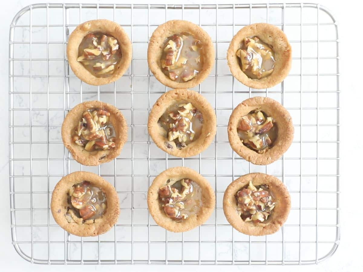 cookie cups on rack with caramel and pecans inside