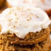 A close-up of pumpkin cookies stacked on top of each other, these delicious pumpkin cookies are topped with creamy white frosting and sprinkled with cinnamon.