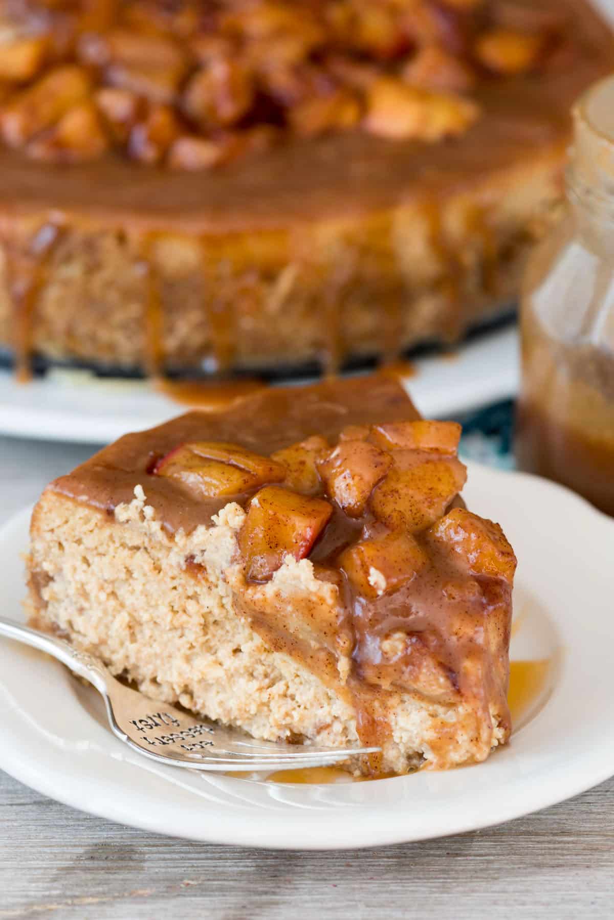 a slice cheesecake with apples baked on top on a white plate