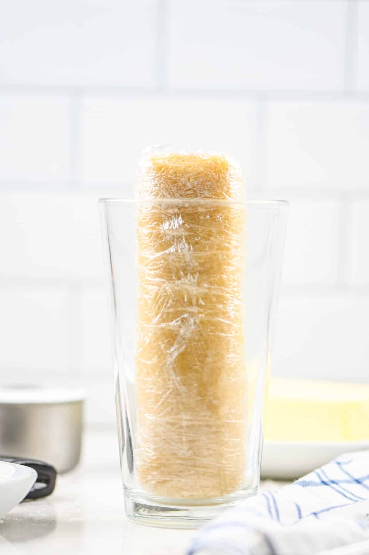 cookie dough log wrapped in plastic in a glass