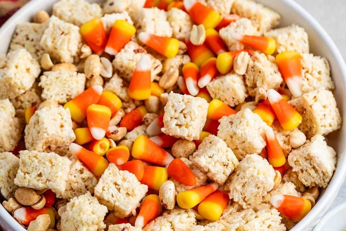 A bowl filled with rice crispy treat squares, candy corn, and peanuts, creating a colorful and festive Halloween Snack Mix.