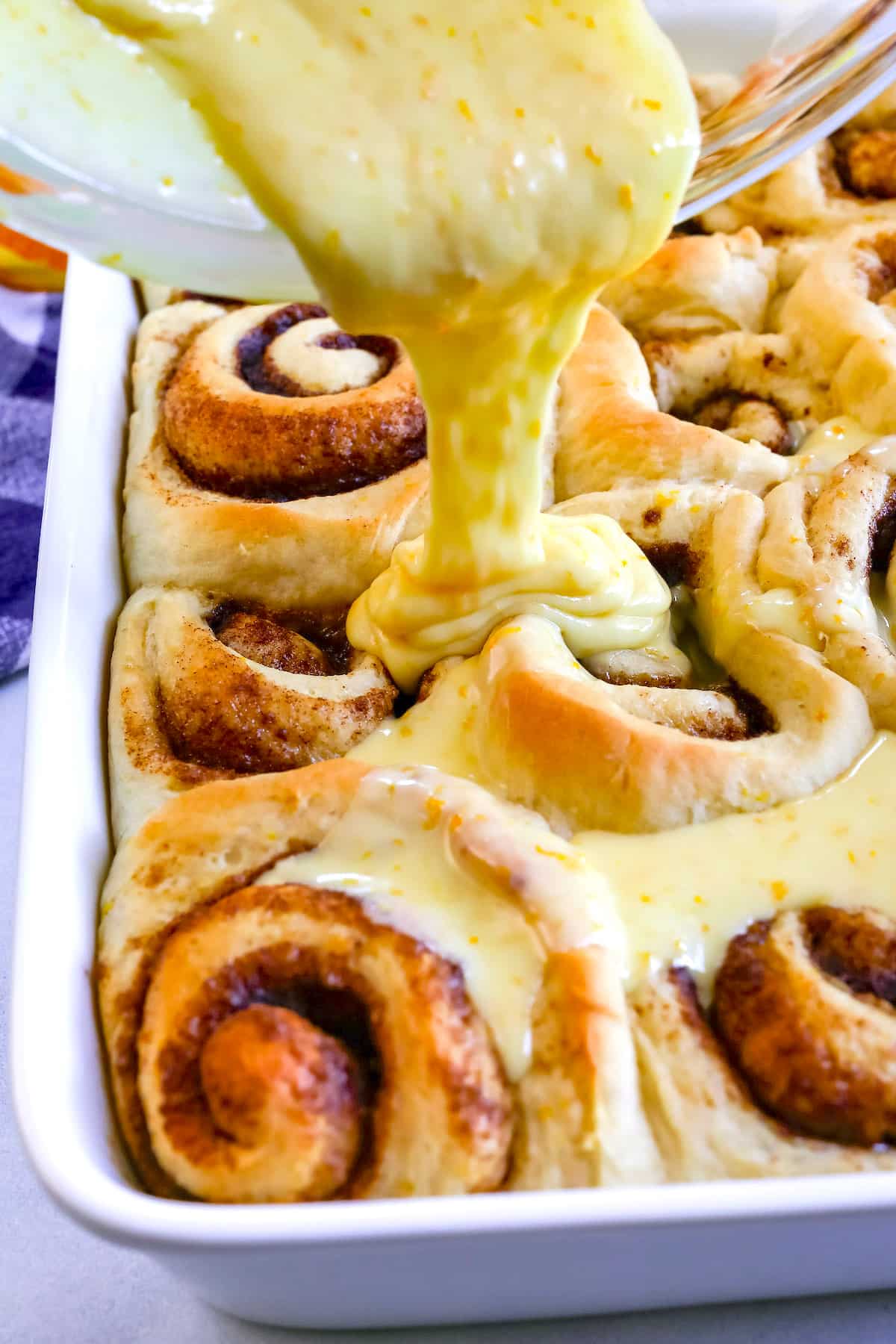 sweet rolls with frosting being poured out of a clear bowl onto the sweet rolls