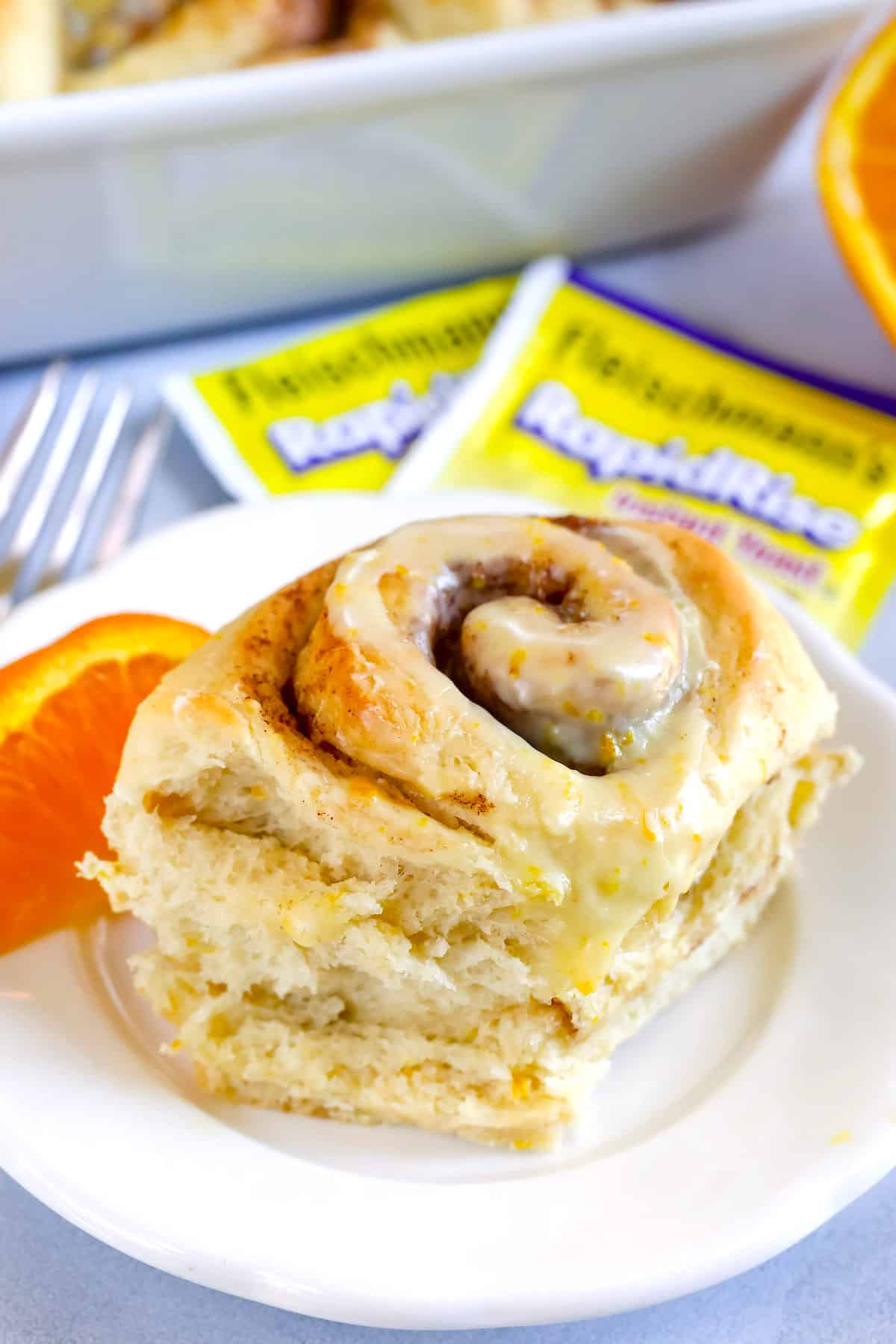 one sweet roll placed on a white plate next to a orange