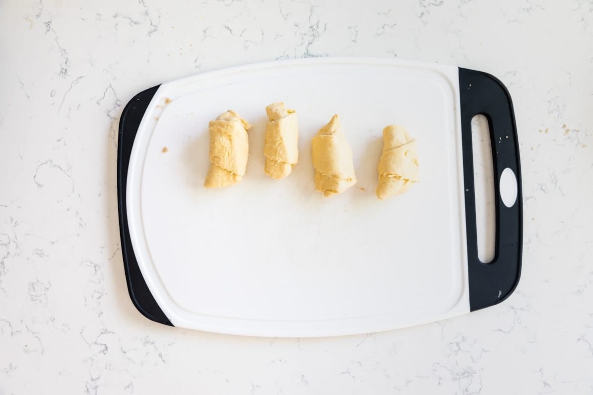 4 rolled up crescent rolls on white cutting board.