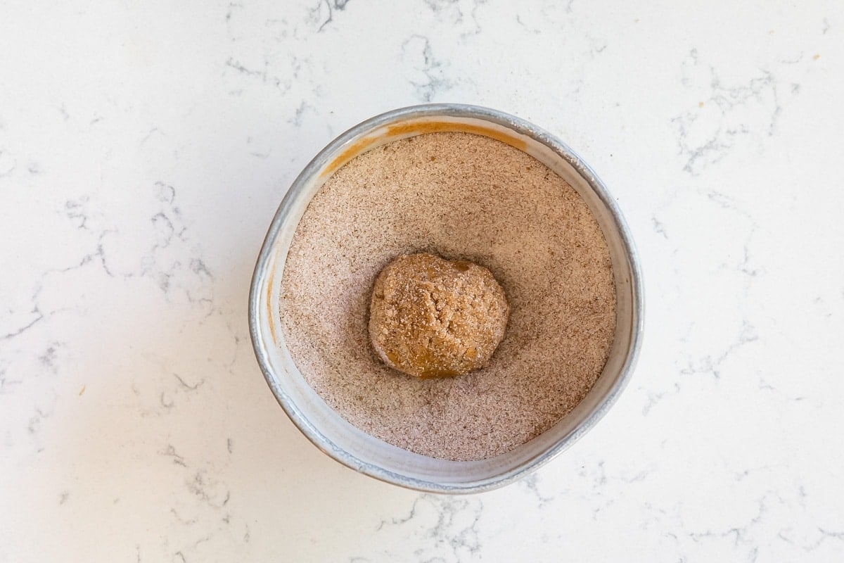 cookie dough ball being rolled in cinnamon sugar.