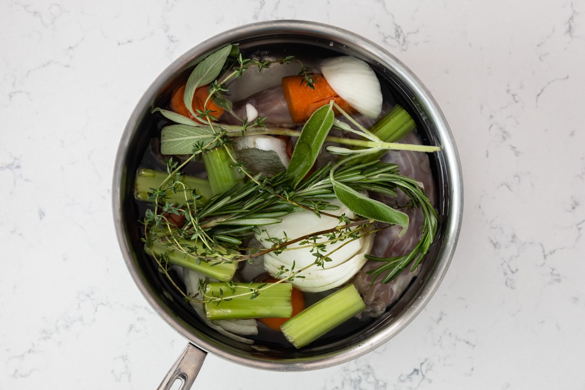 stock and vegetables and herbs in pot.