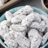 muddy buddies covered in powdered sugar in a blue bowl with words on top