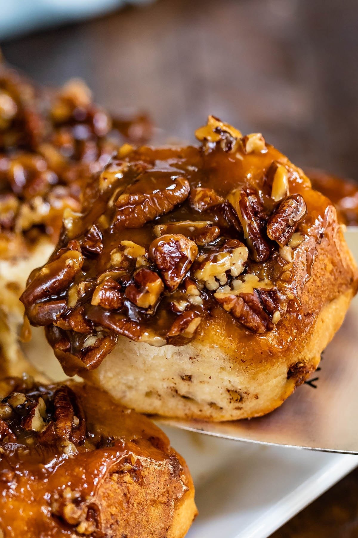 one sticky bun being lifted out of a white baking plan