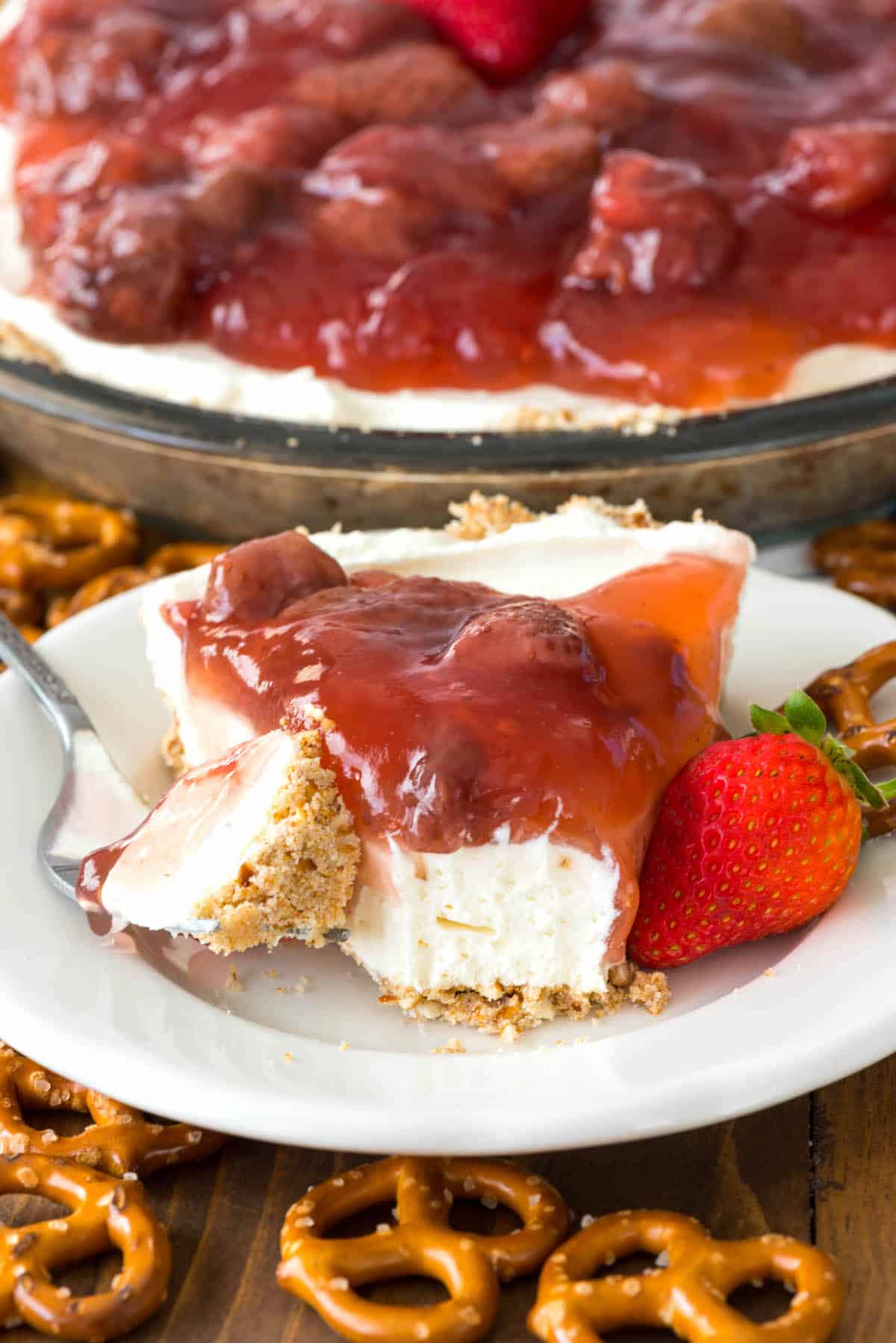 slice of cream cheese pie on white plate with strawberry topping with bite missing