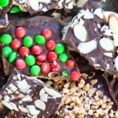 Assorted pieces of chocolate toffee bark and graham cracker toffee, topped with red and green candy-coated chocolates, sliced almonds, and crushed toffee pieces. The treats are arranged in a festive, colorful pile.