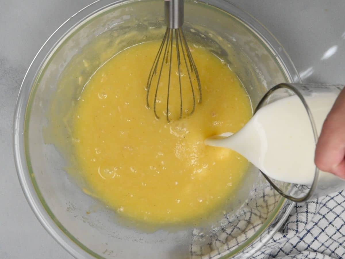 bowl of buttermilk pie mixture with measuring cup pouring in buttermilk