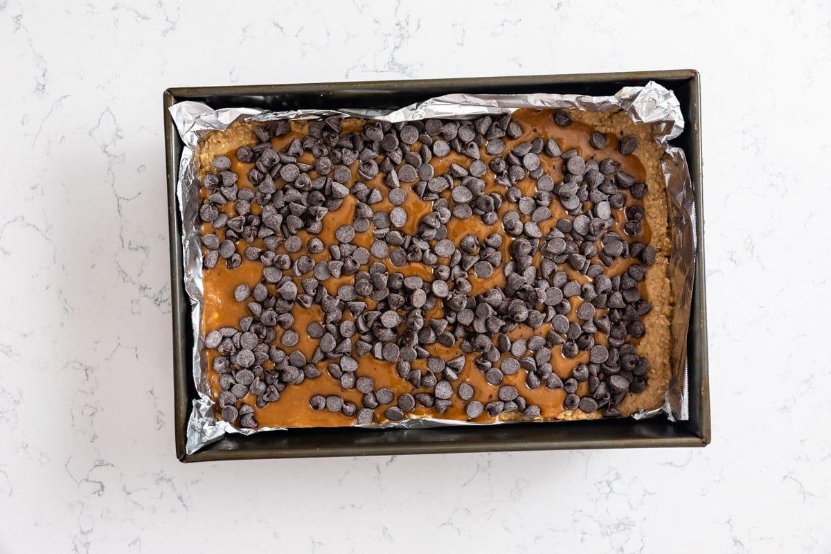 cookie dough in pan with caramel and chocolate chips.