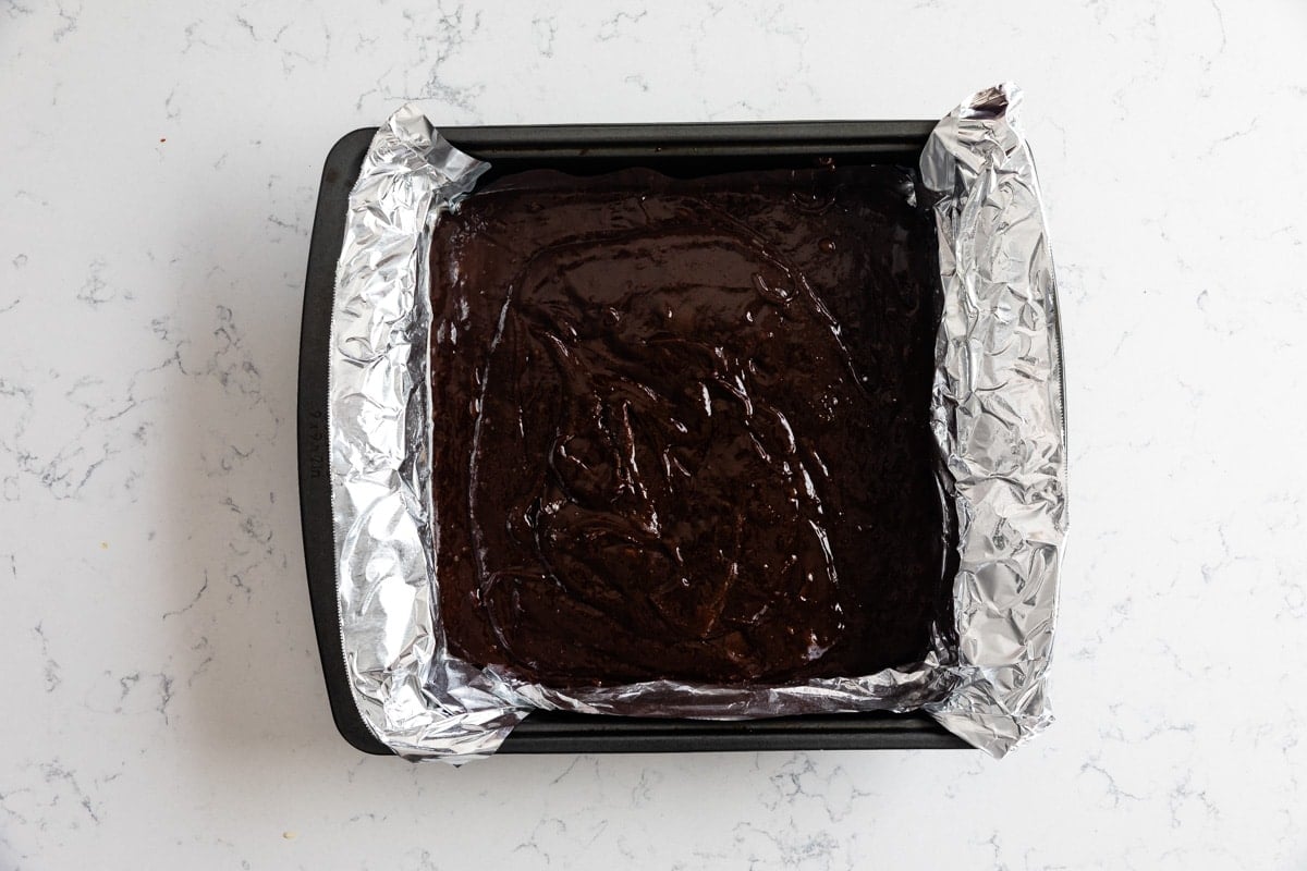 brownie batter in square pan with foil.