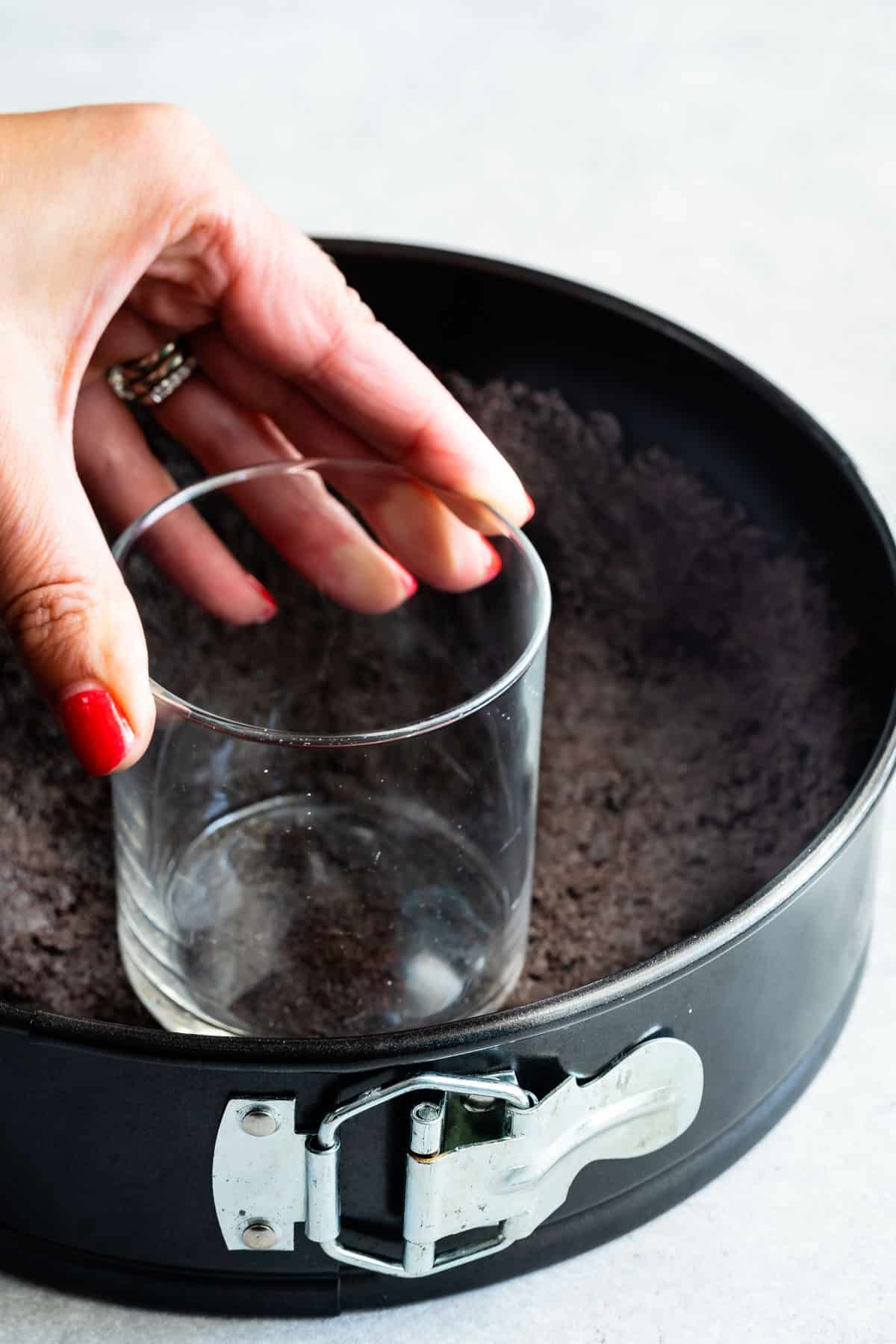 hand holding glass pressing crust in springform pan.