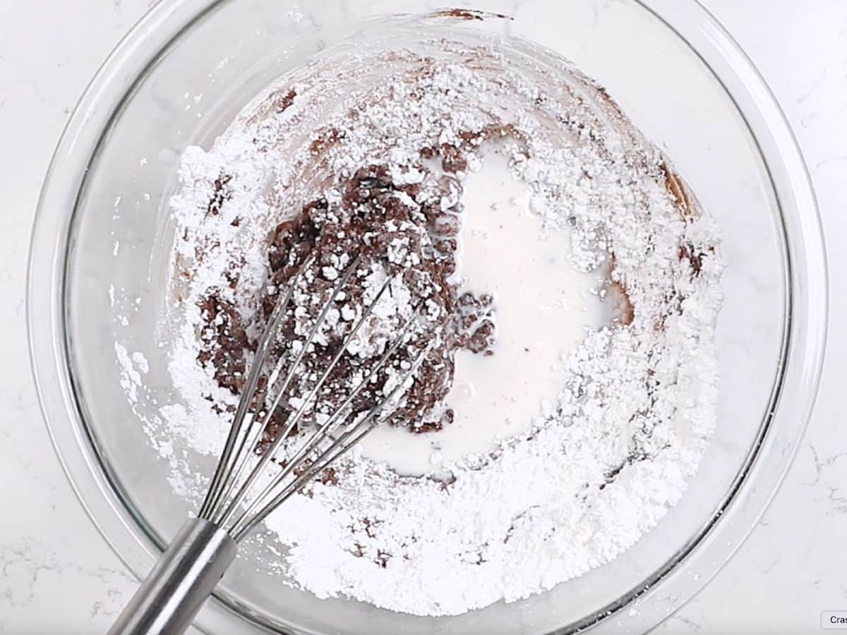 icing being made - powdered sugar cocoa and milk in bowl with whisk.