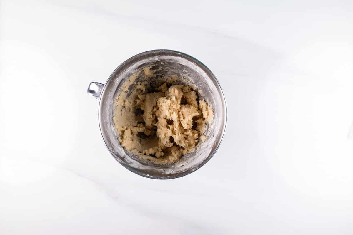 Overhead view of a mixing bowl with cookie dough inside, ready to be transformed into a delicious shortbread cookies recipe on a white marble surface.
