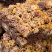Close-up of homemade pecan pie brownies stacked on top of each other, showing a crumbly, golden-brown texture with visible pecan pieces inside.