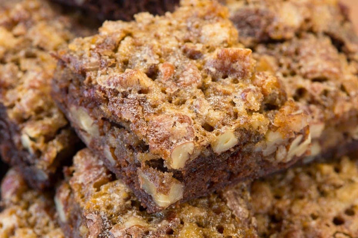 Close-up of homemade pecan pie brownies stacked on top of each other, showing a crumbly, golden-brown texture with visible pecan pieces inside.