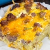 A slice of hashbrown breakfast casserole on a white plate, topped with melted cheese and pieces of sausage.