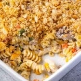 A close-up of a turkey casserole baked pasta with a golden breadcrumb topping in a white dish, showing spiral noodles, pieces of turkey and chicken, and mixed vegetables.