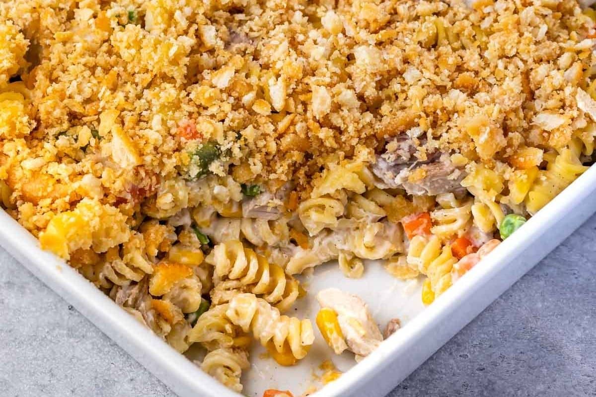 A close-up of a turkey casserole baked pasta with a golden breadcrumb topping in a white dish, showing spiral noodles, pieces of turkey and chicken, and mixed vegetables.