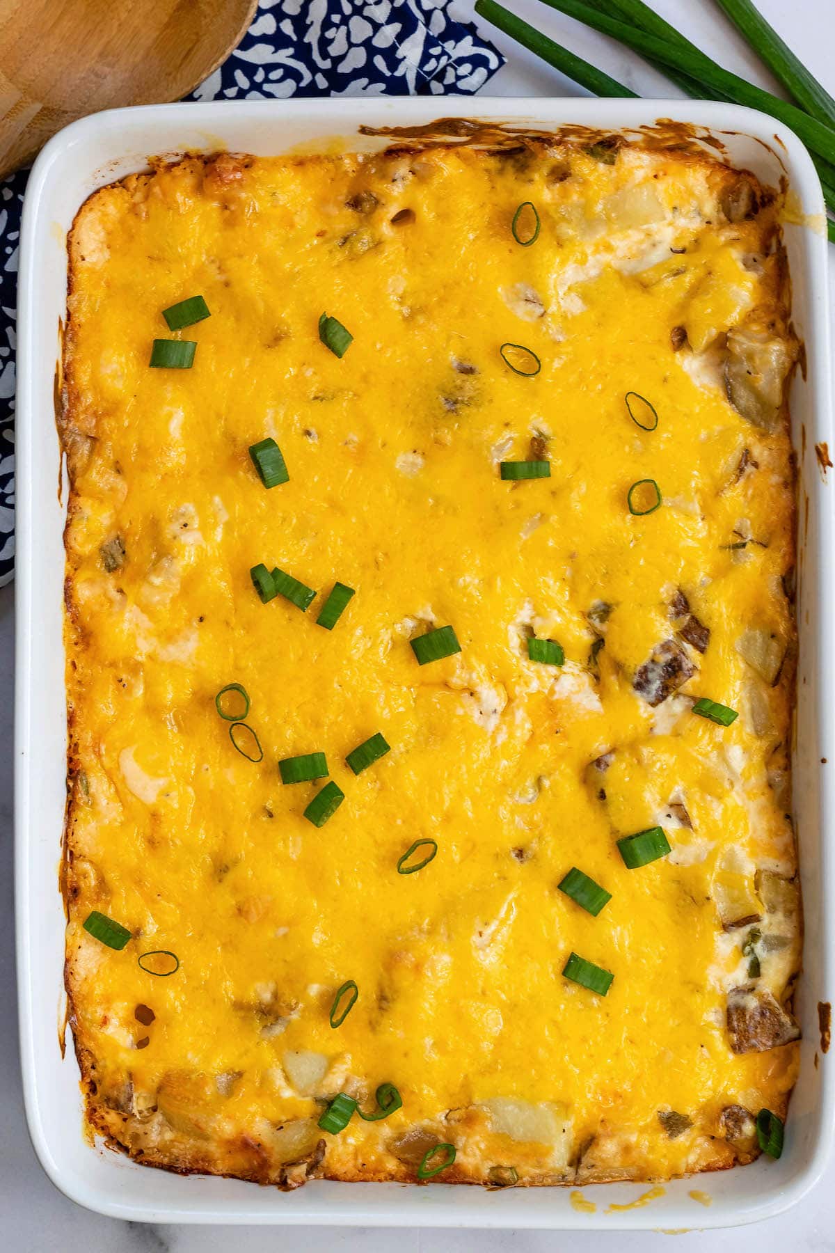 casserole layered with cheese in a white pan next to a wooden spoon