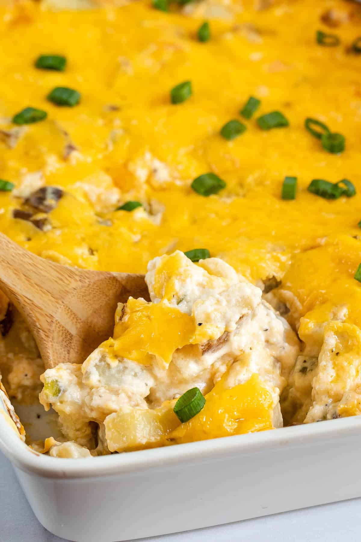 casserole layered with cheese in a white pan next to a wooden spoon