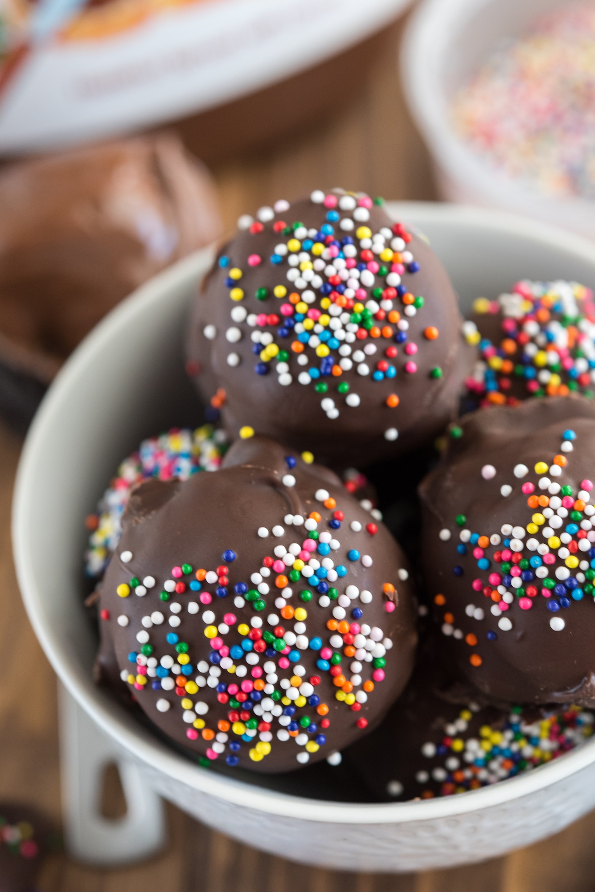 chocolate covered truffled with colorful sprinkles on top in a white bowl