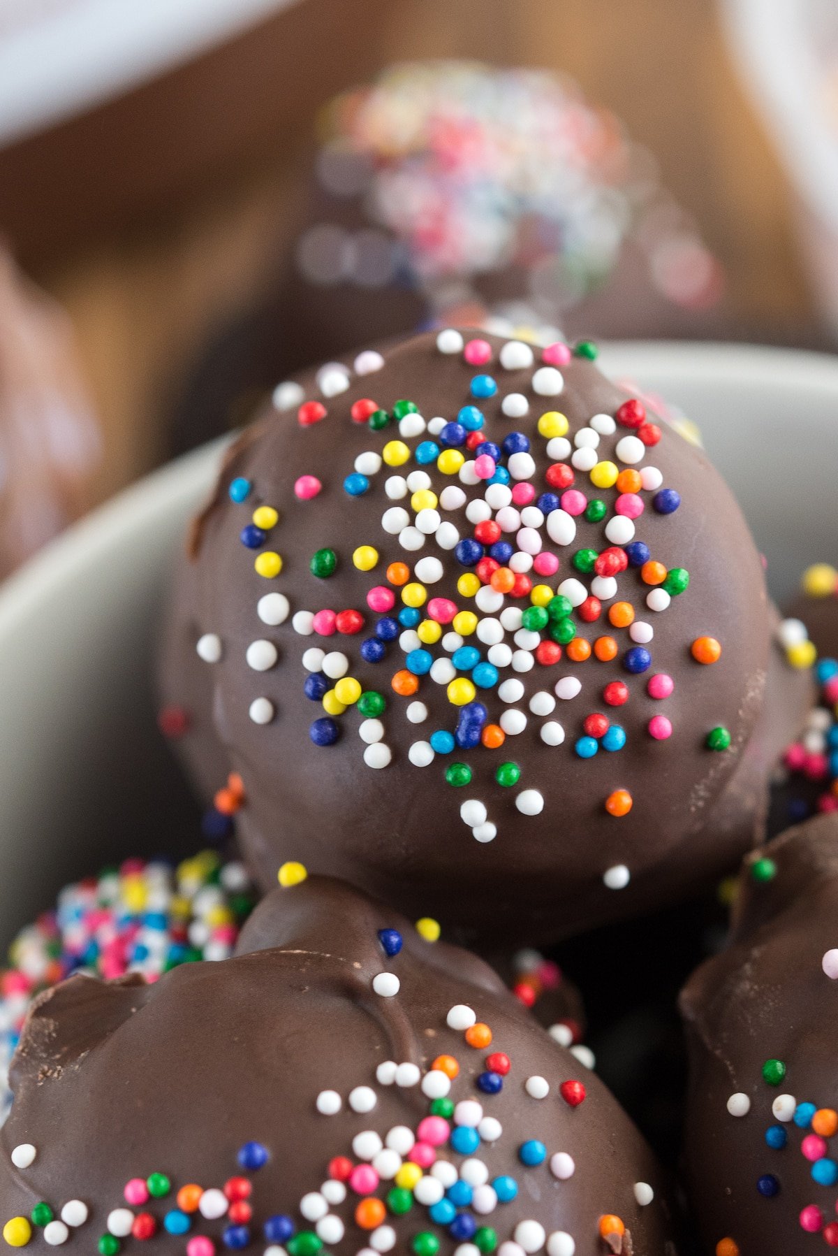 chocolate covered truffled with colorful sprinkles on top in a white bowl