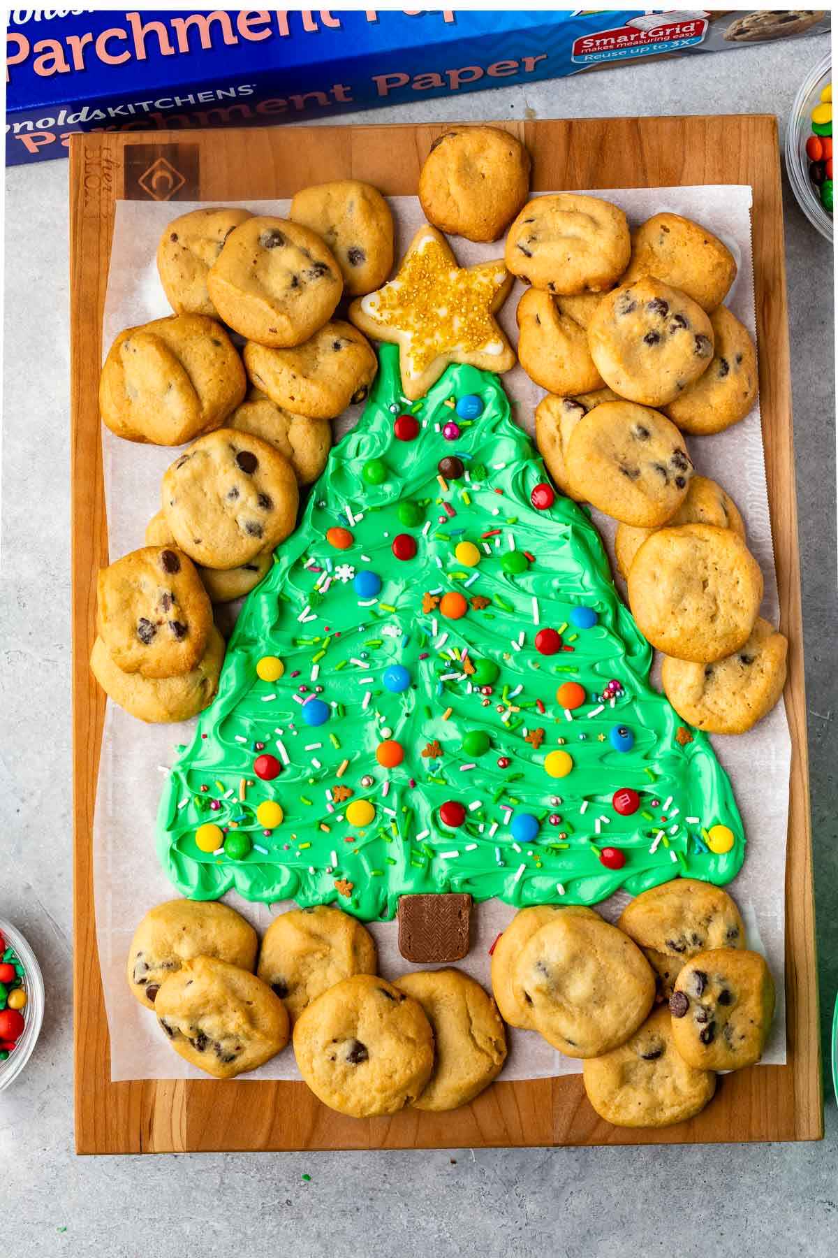 frosting on board decorated like a christmas tree surrounded by mini chocolate chip cookies