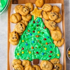 frosting on board decorated like a christmas tree surrounded by mini chocolate chip cookies