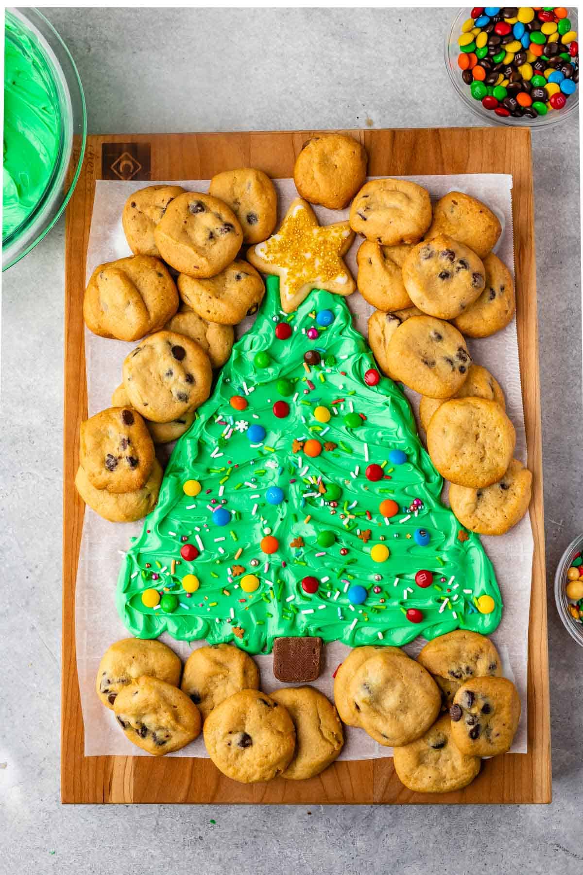 frosting on board decorated like a christmas tree surrounded by mini chocolate chip cookies
