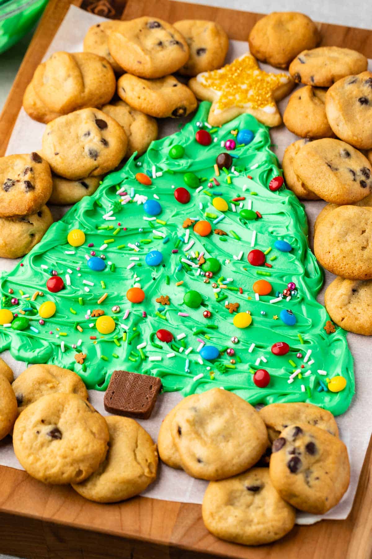 frosting on board decorated like a christmas tree surrounded by mini chocolate chip cookies