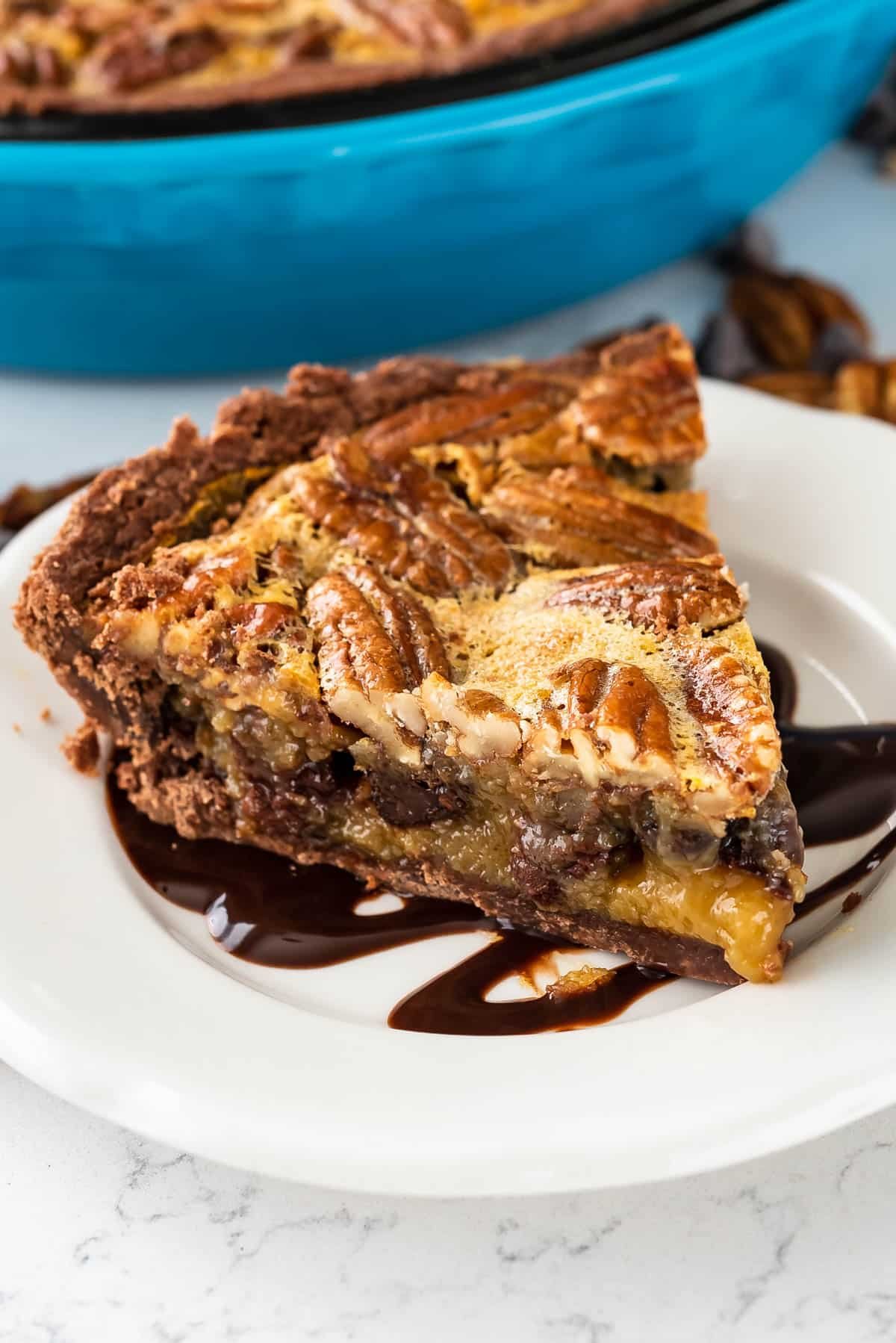 pecan chocolate pie on a white plate with chocolate drizzled over the top