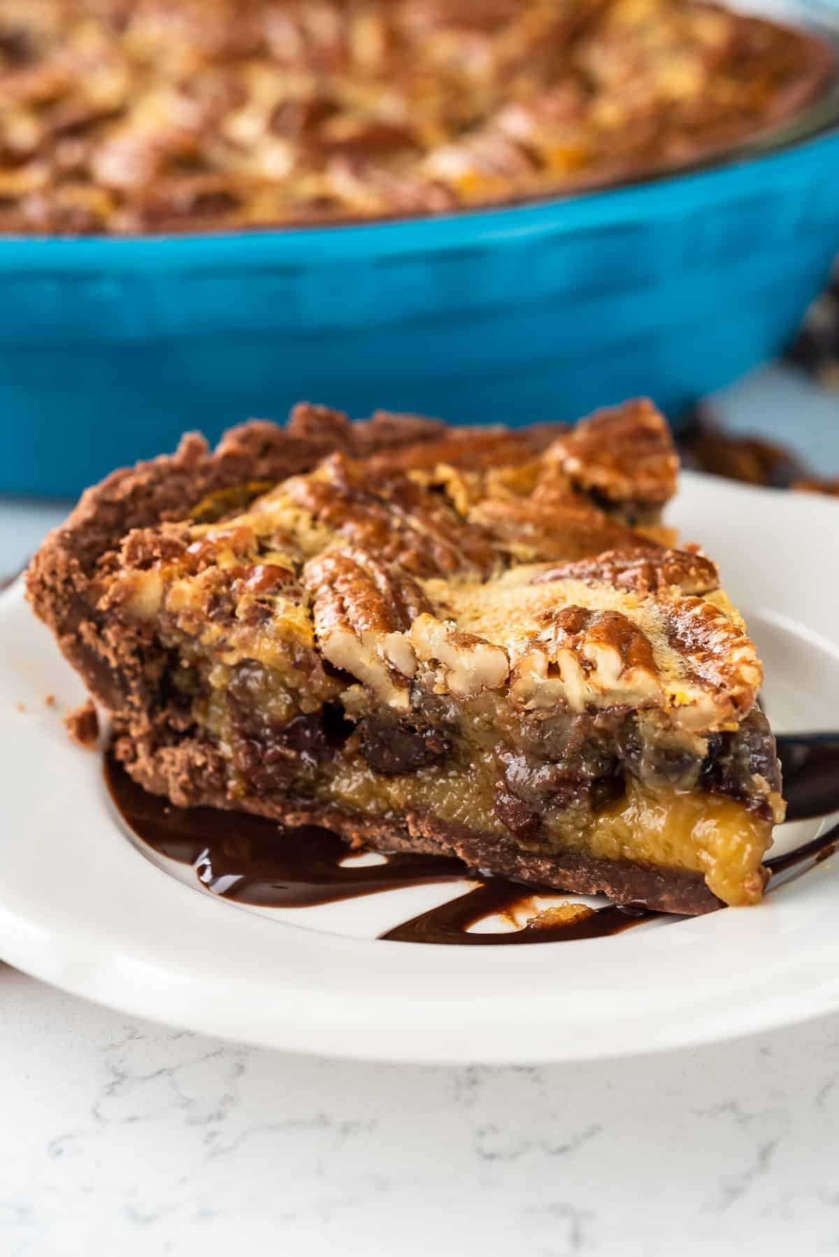 pecan chocolate pie on a white plate with chocolate drizzled over the top
