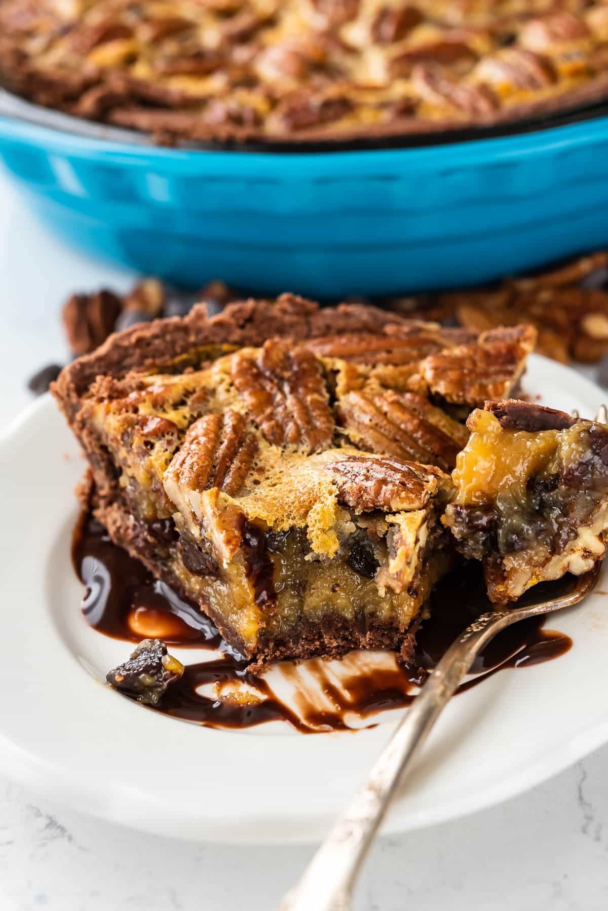 pecan chocolate pie on a white plate with a bite taken out.