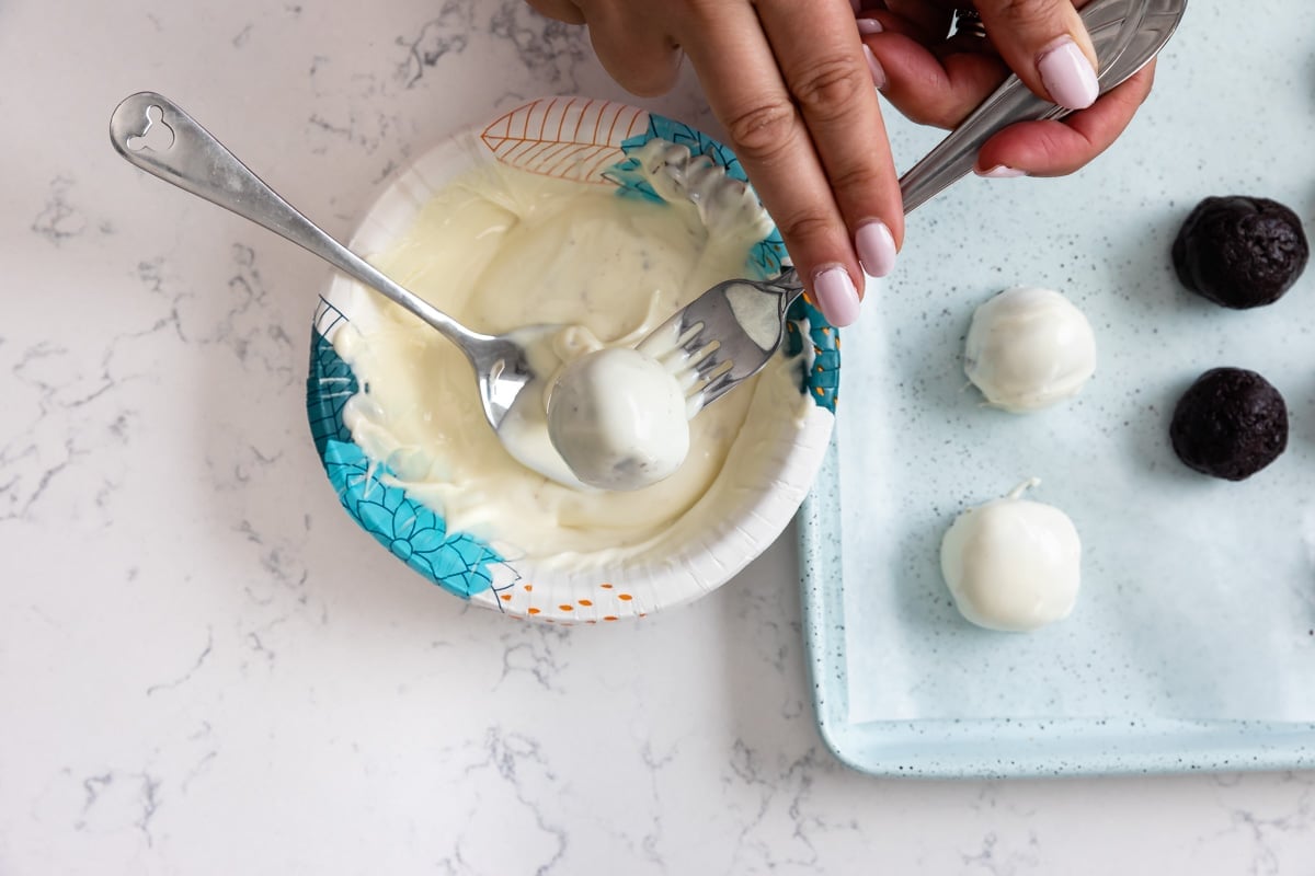 Oreo ball being dipped in bowl of melted white chocolate.