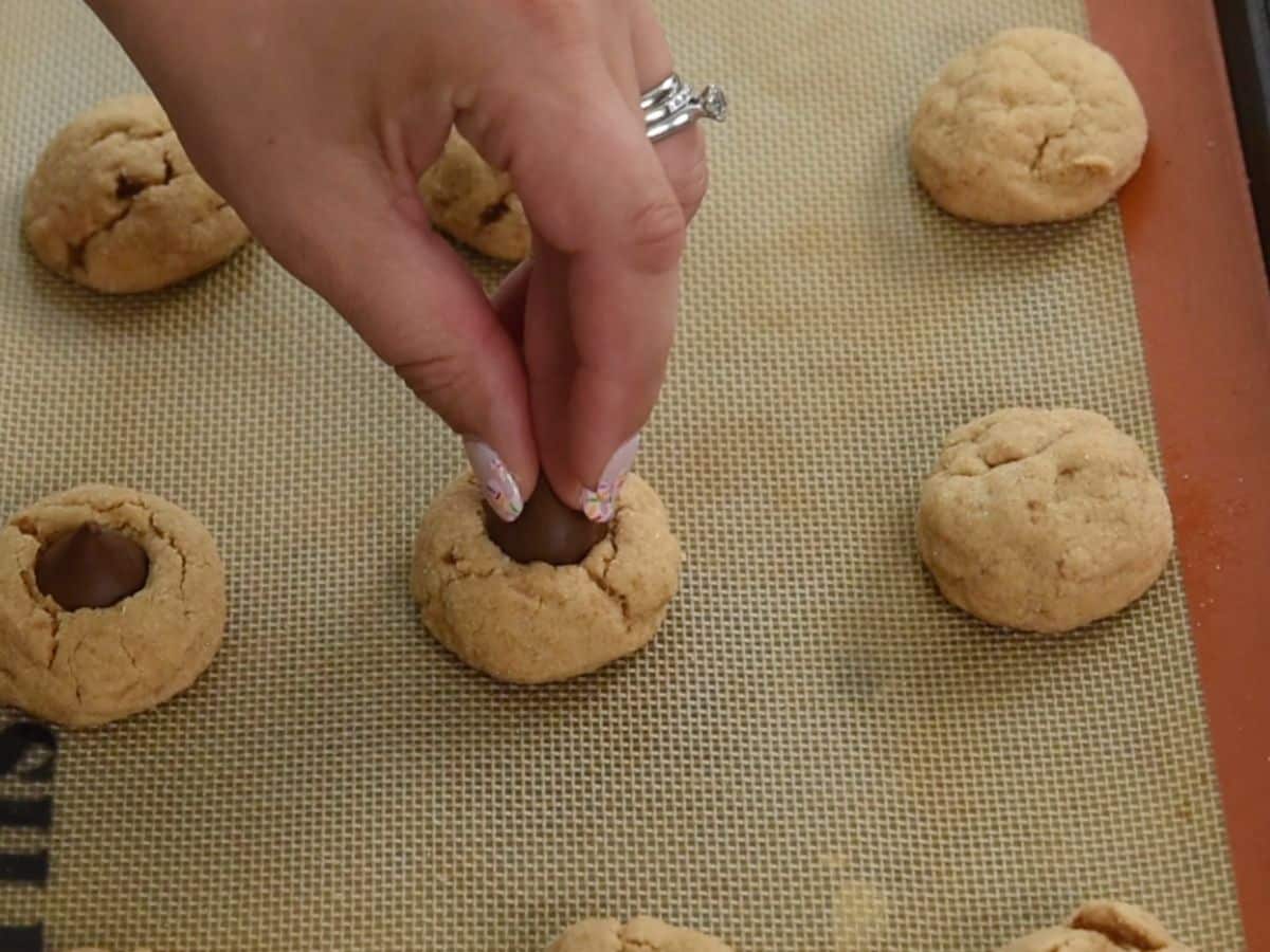 hand pressing Hershey kiss into a peanut butter cookie.