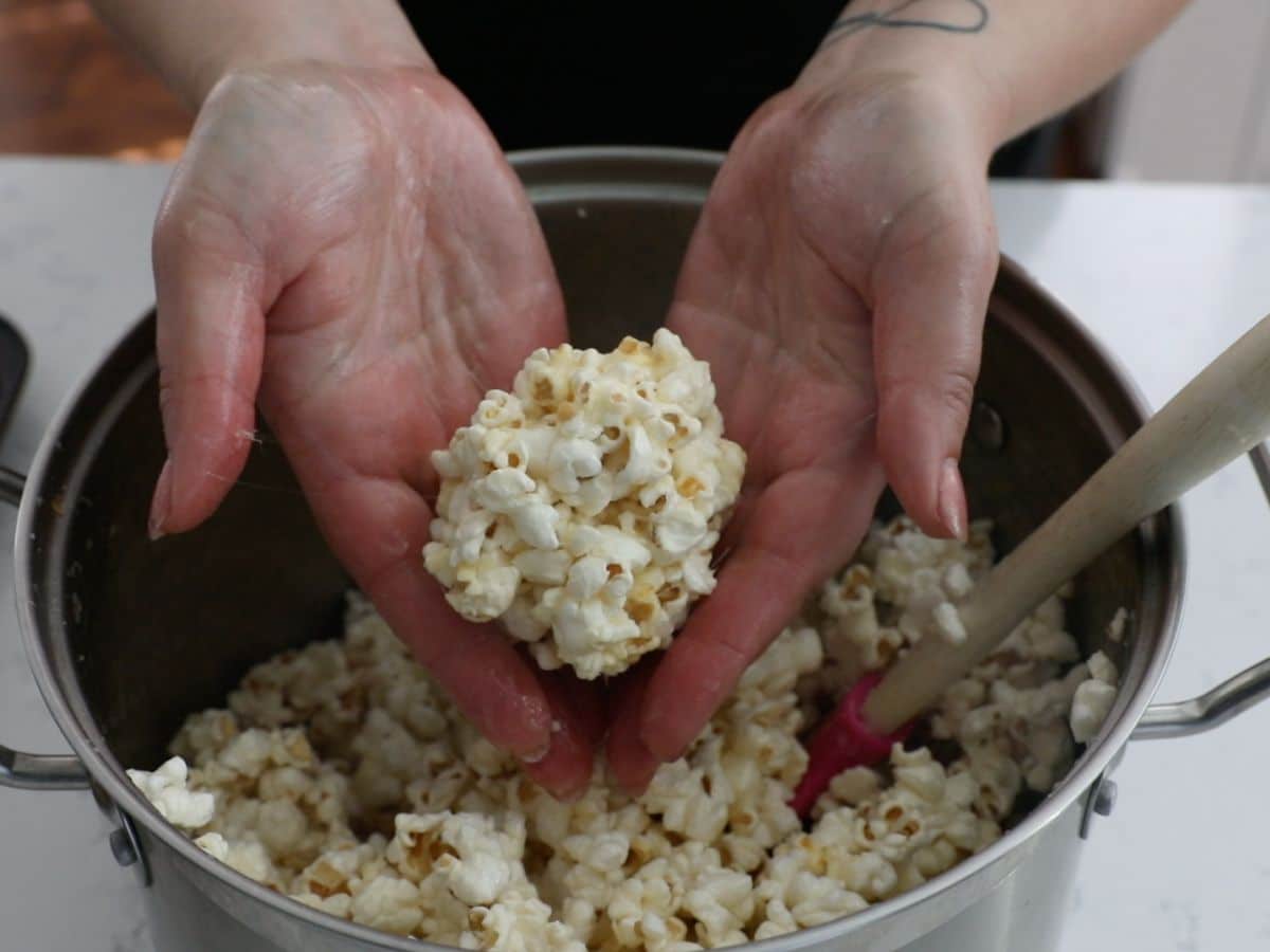 hands forming popcorn ball over pot of popcorn.