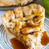 slice of apple pie with lattice top drizled with caramel on white plate with blue stripes