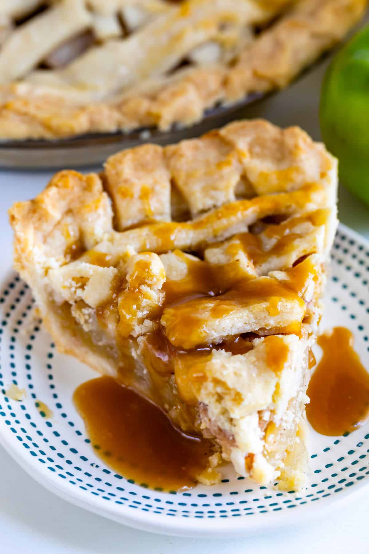 slice of apple pie with lattice top drizled with caramel on white plate with blue stripes