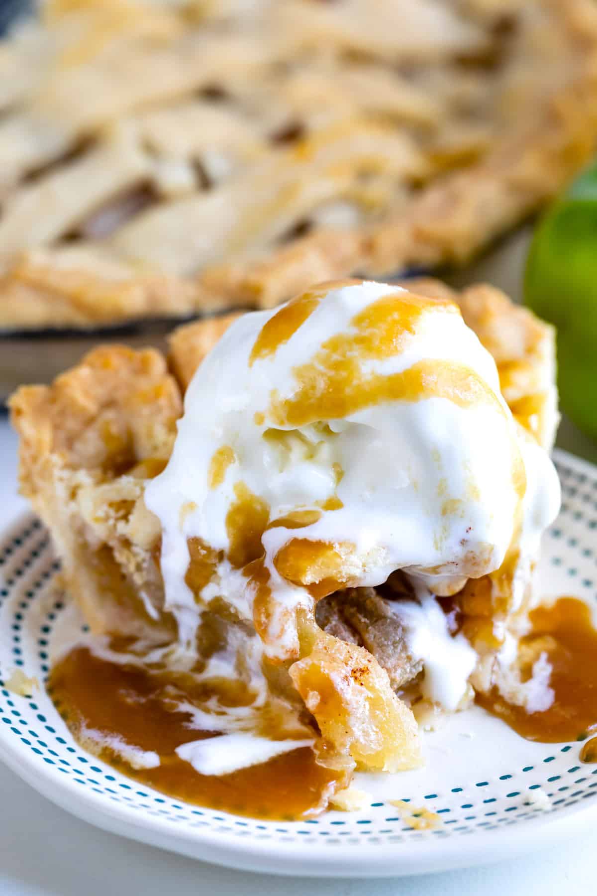 slice of apple pie ala mode with lattice top on white plate with blue stripes with bite missing