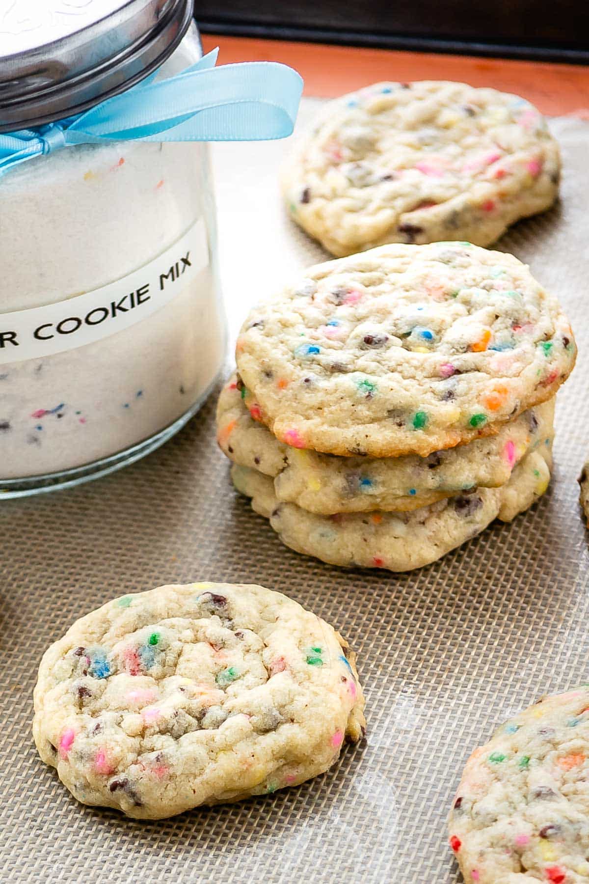 two photos of sugar cookie mix in a big clear container with sugar cookies sitting around the container