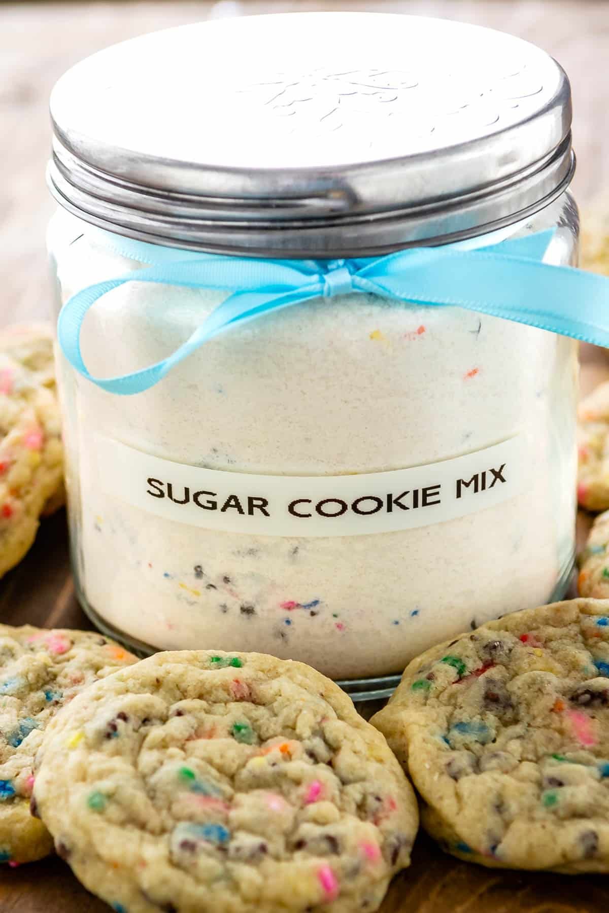 two photos of sugar cookie mix in a big clear container with sugar cookies sitting around the container
